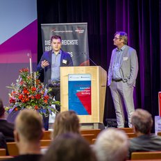 Zwei Männer halten auf der Bühne einen Vortrag.