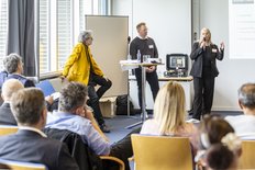 Zwei Personen halten einen Vortrag vor vielen sitzenden Teilnehmenden